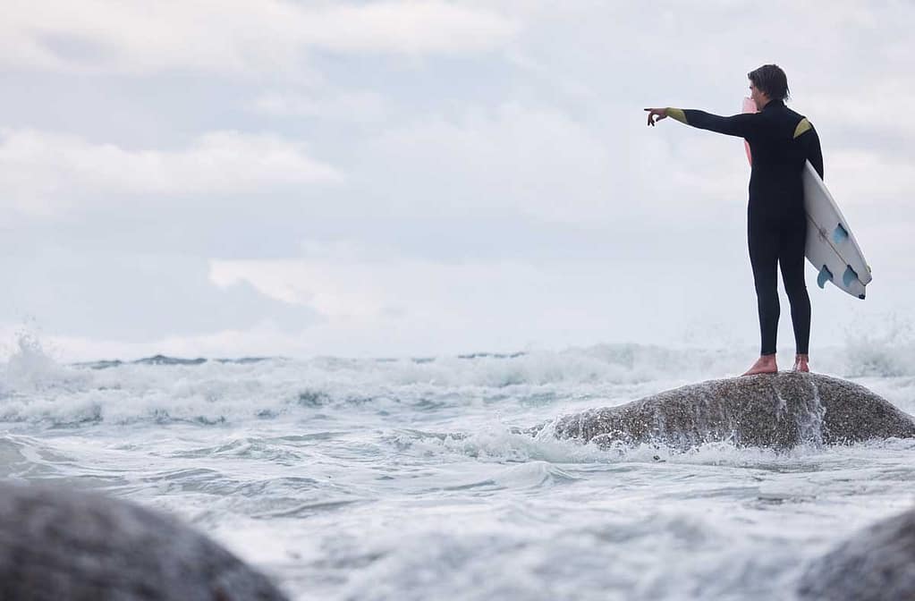 Man Pointing Or Surfer On Rocks At Beach Ocean